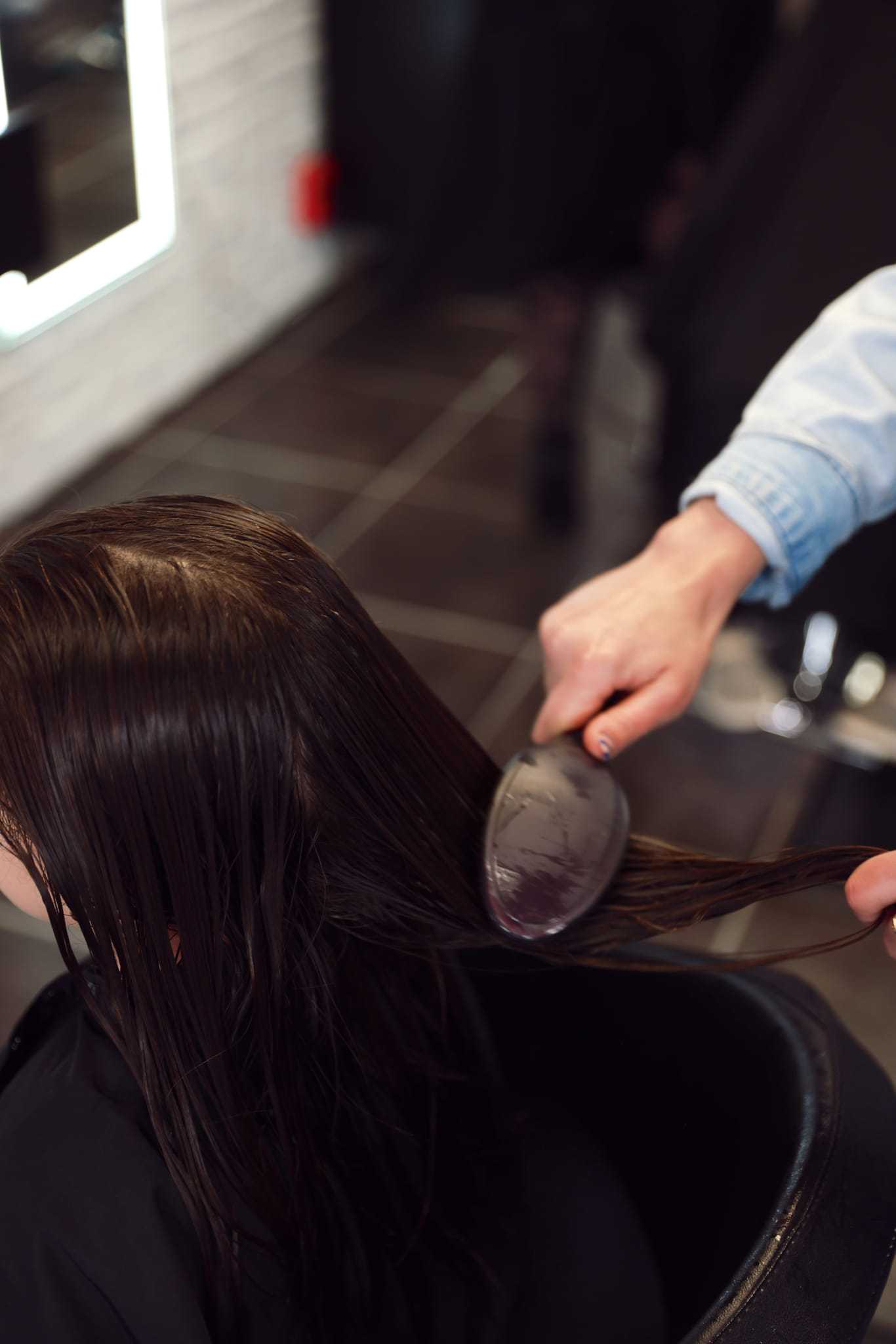Hairdresser brushing wet hair in a salon setting.
